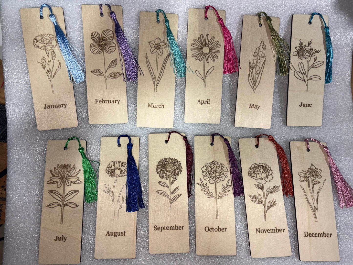 Wooden bookmarks with floral designs and months engraved, each with a colorful tassel.