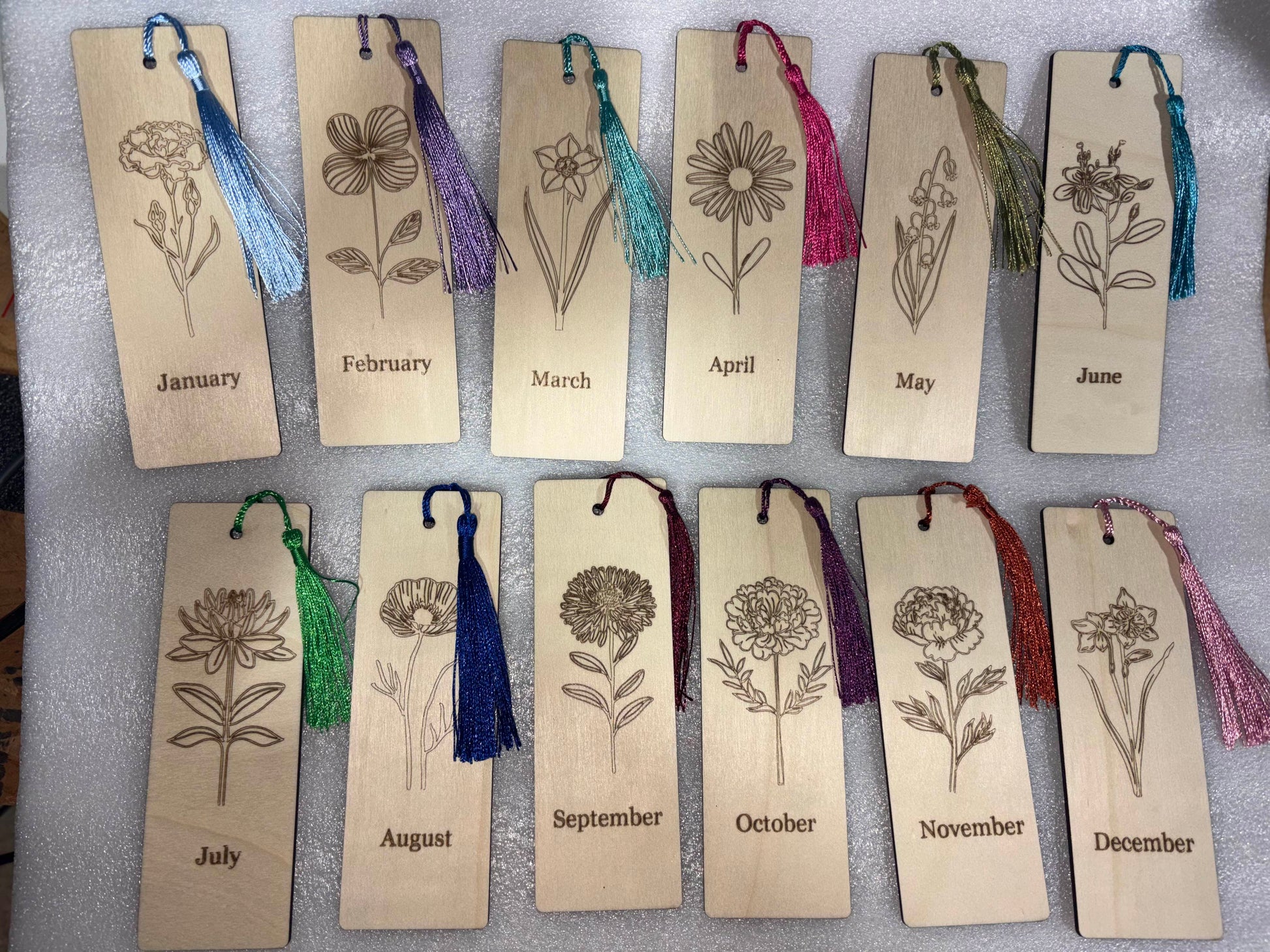 Wooden bookmarks with floral designs and months engraved, each with a colorful tassel.