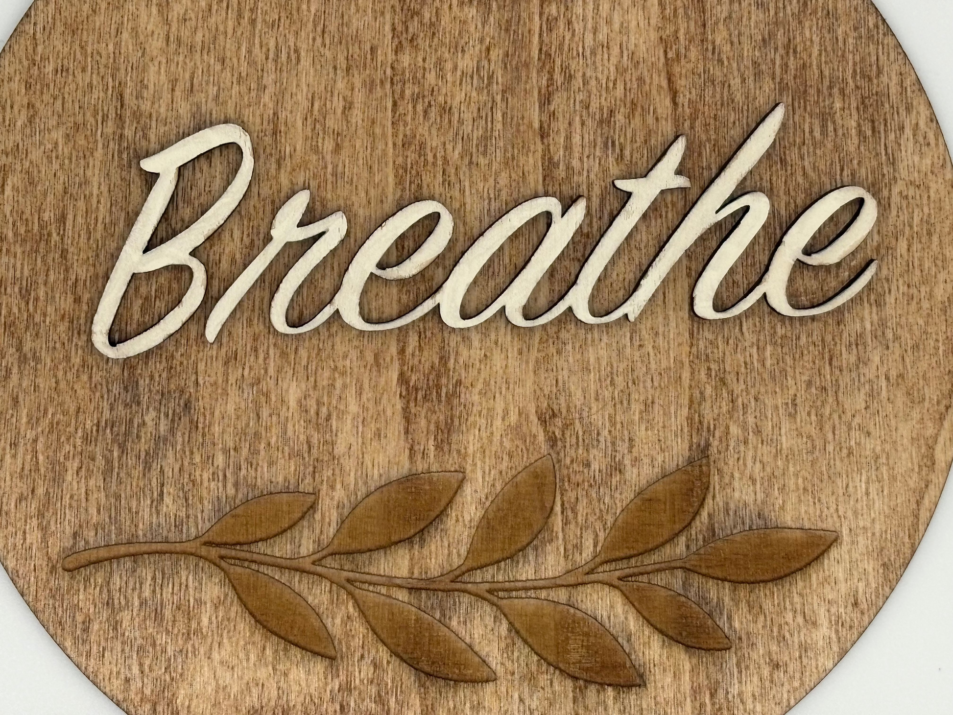 Wooden circular sign with leaf design and 'Breathe' text on a white background