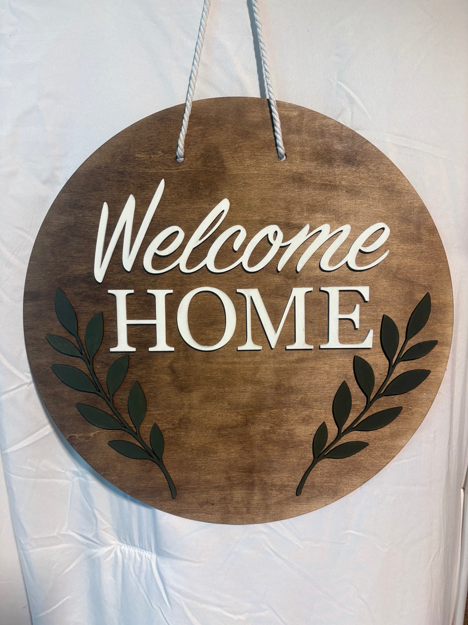 Wooden circular sign with 'Welcome Home' text and leaf designs on a white background