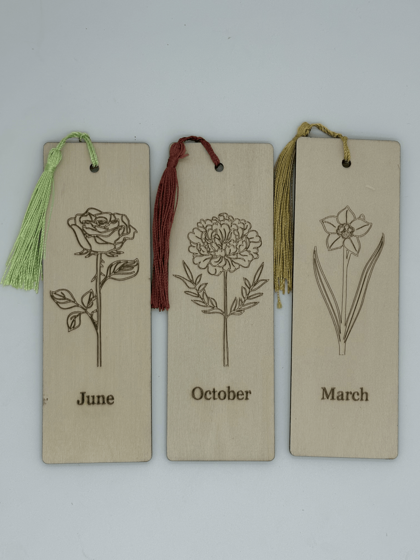 Three bookmarks with floral illustrations and months engraved, each with a tassel.
